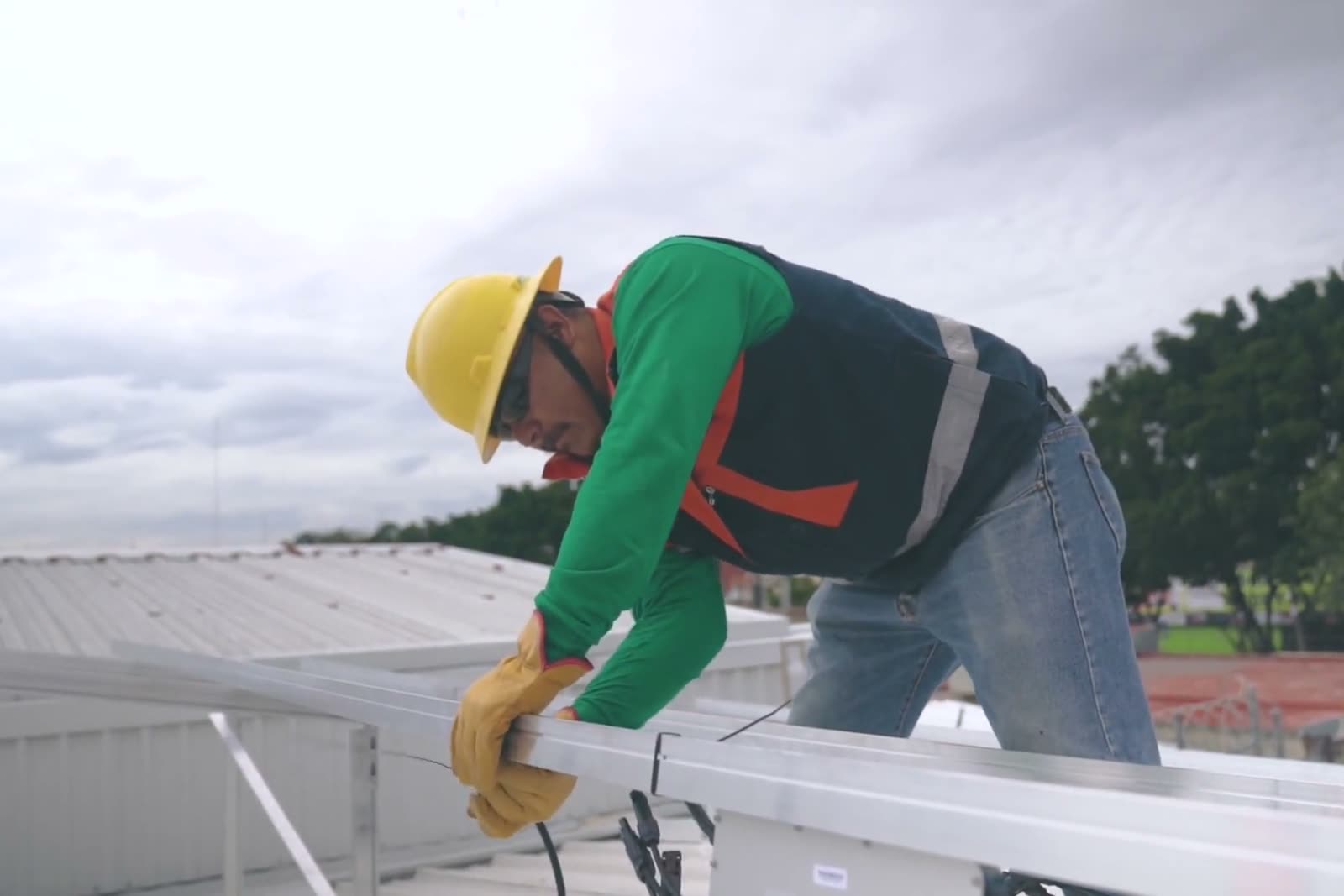 A roofer in a hard hat and gloves fastens framing on a flat commercial roof.